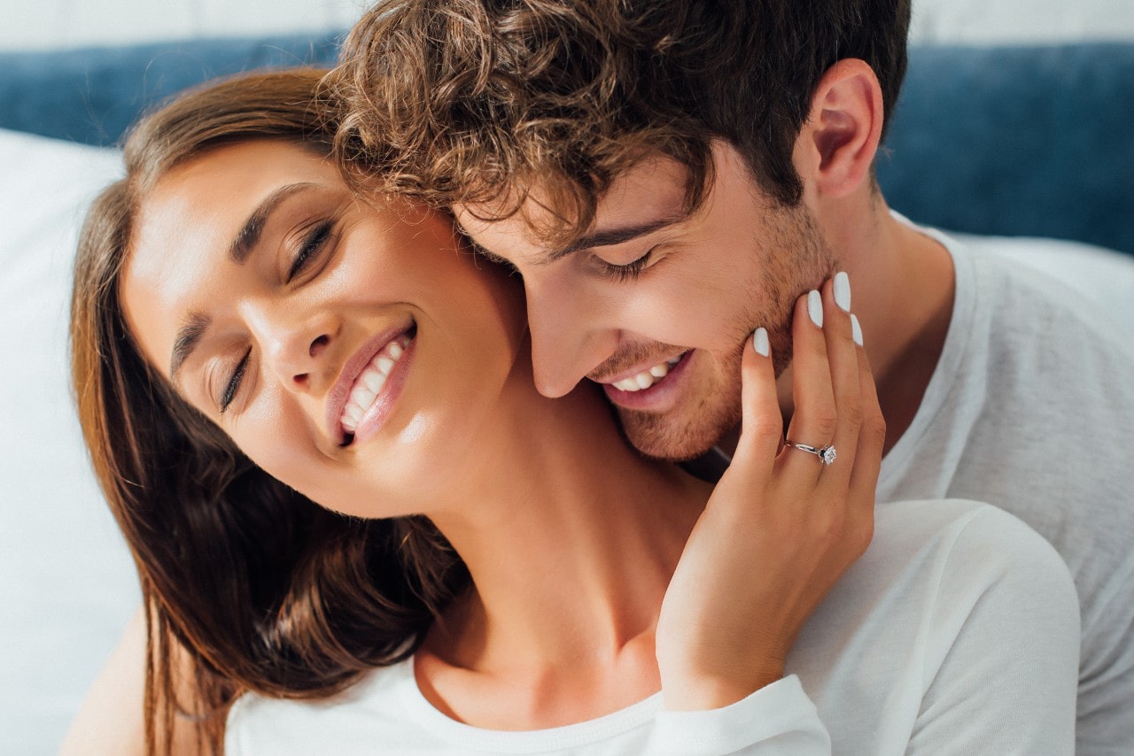 a lady wearing a simple engagement ring and embracing a man