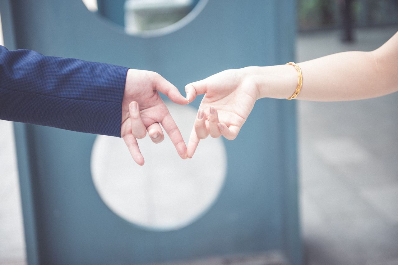 Two people forming a heart with their hands, one of which is wearing a gold bracelet