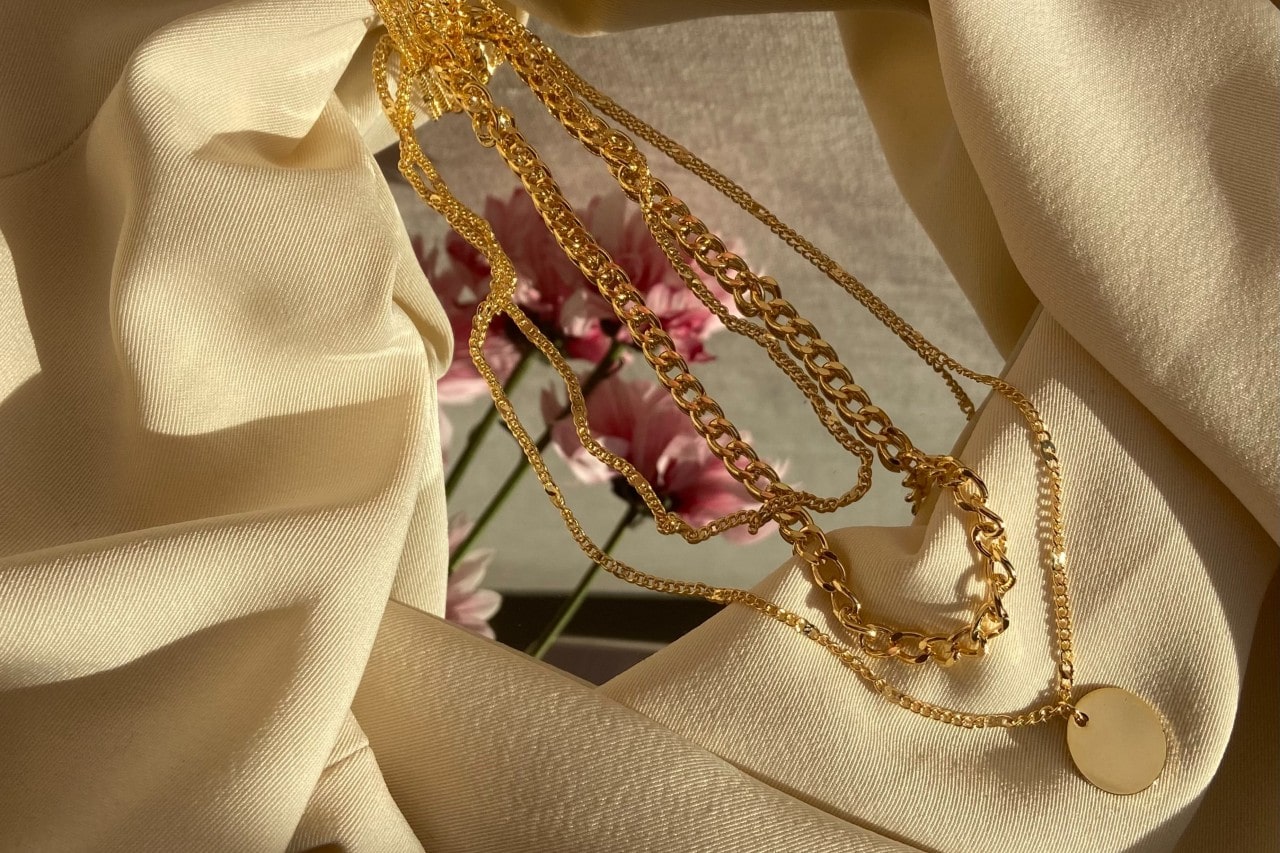 Yellow gold necklace, purple flowers, and a beige blanket