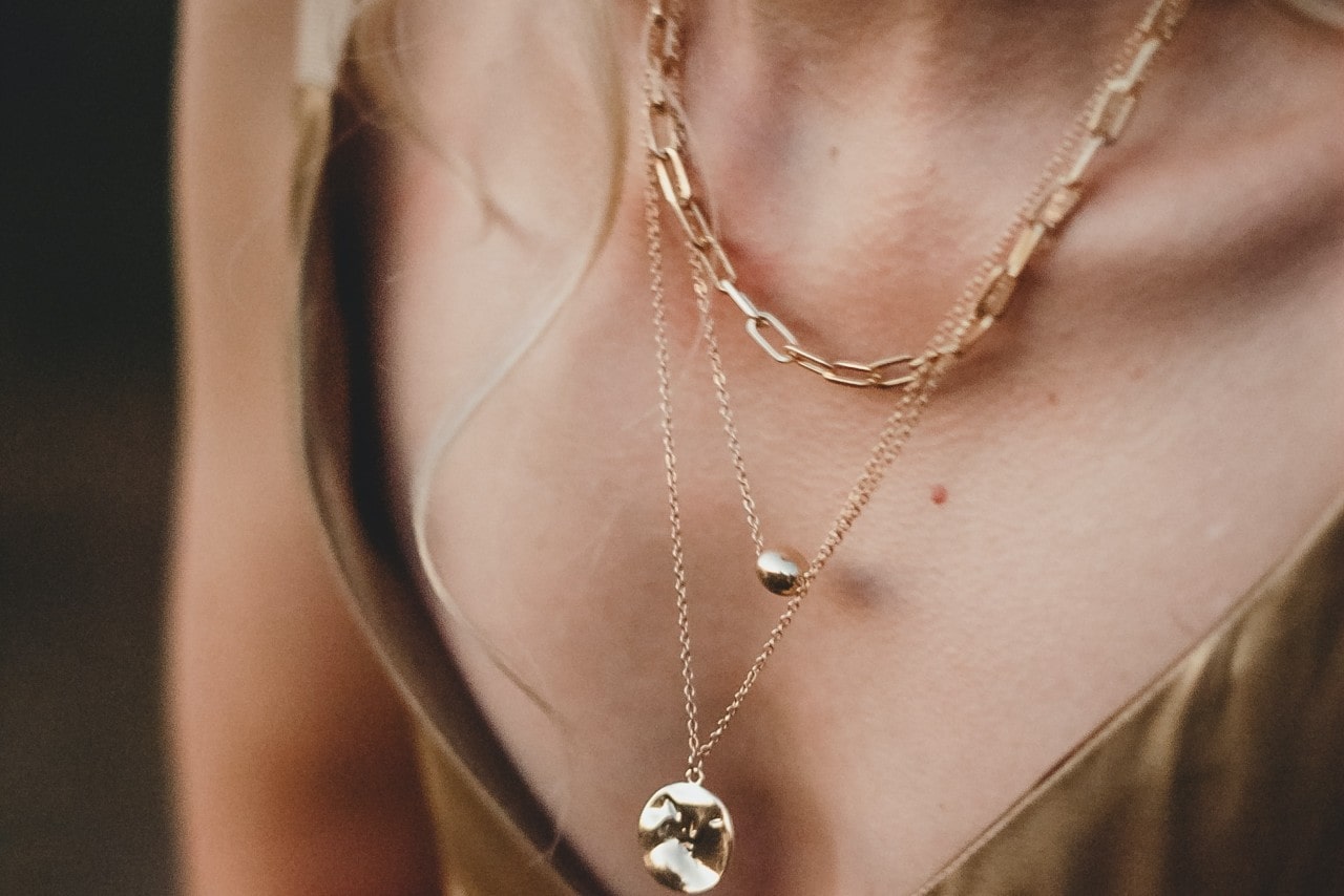 Close up image of a woman’s neckline wearing three gold necklaces of varying lengths