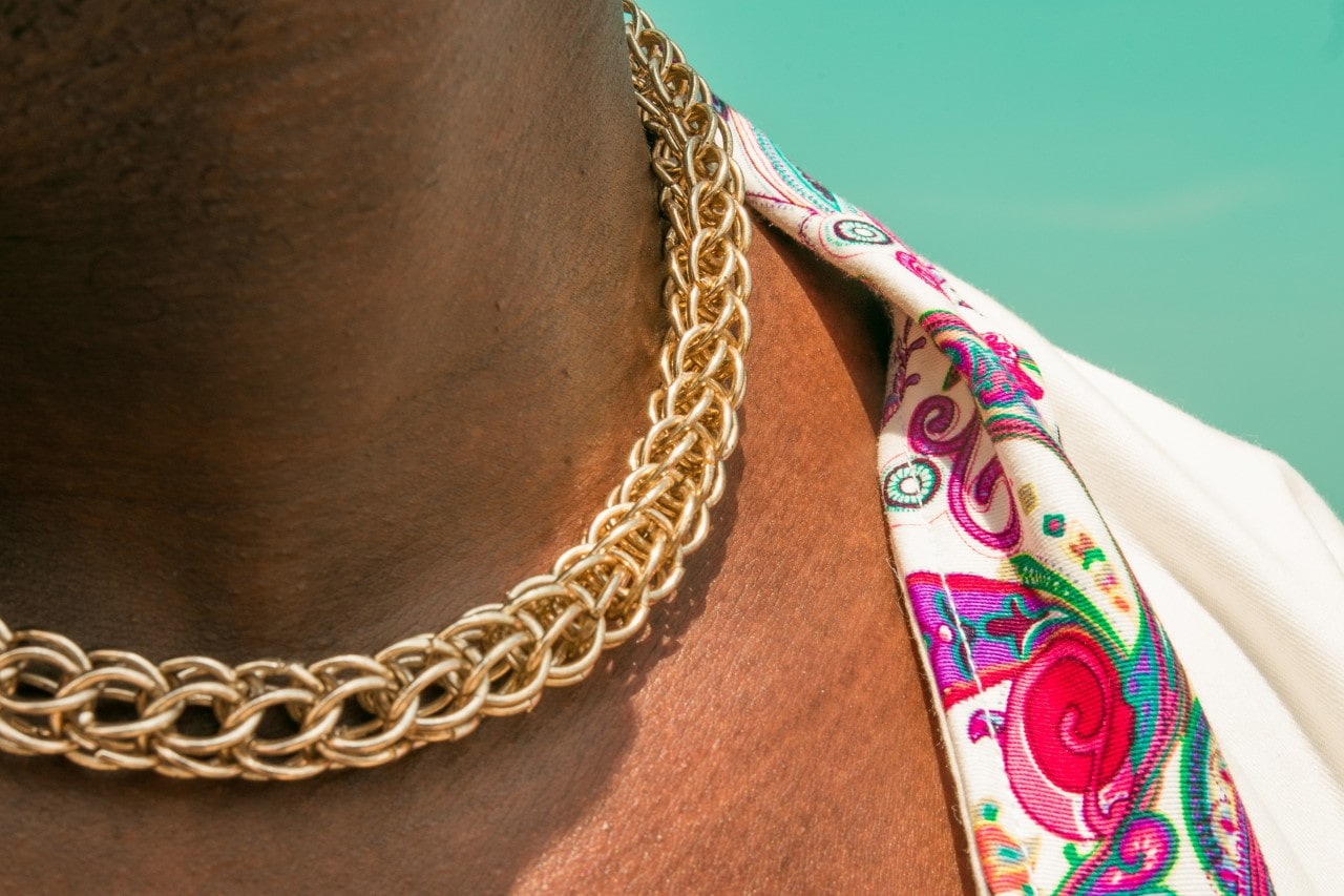 Close up image of a man wearing a gold chain necklace and a colorful shirt