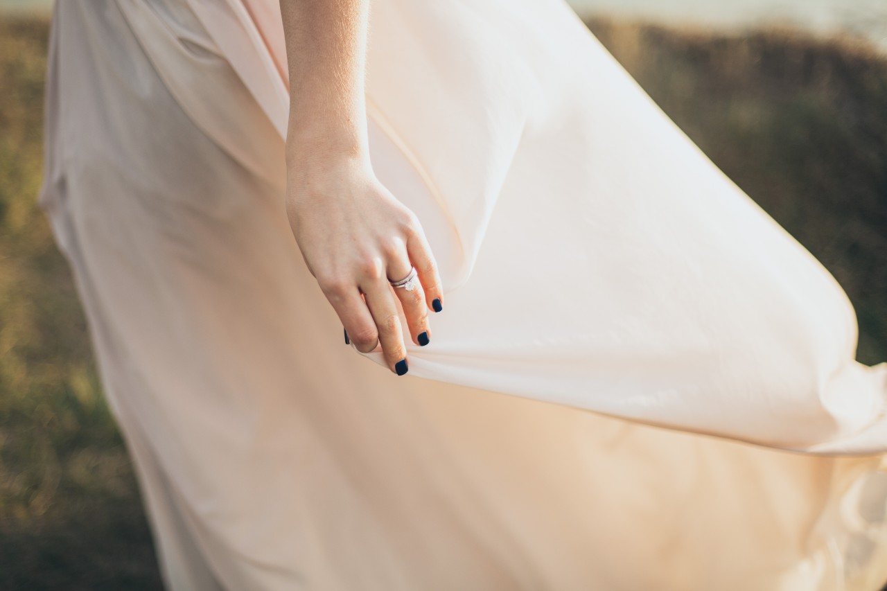 A bride gently holding the skirt of her dress and you can see her engagement ring and wedding band