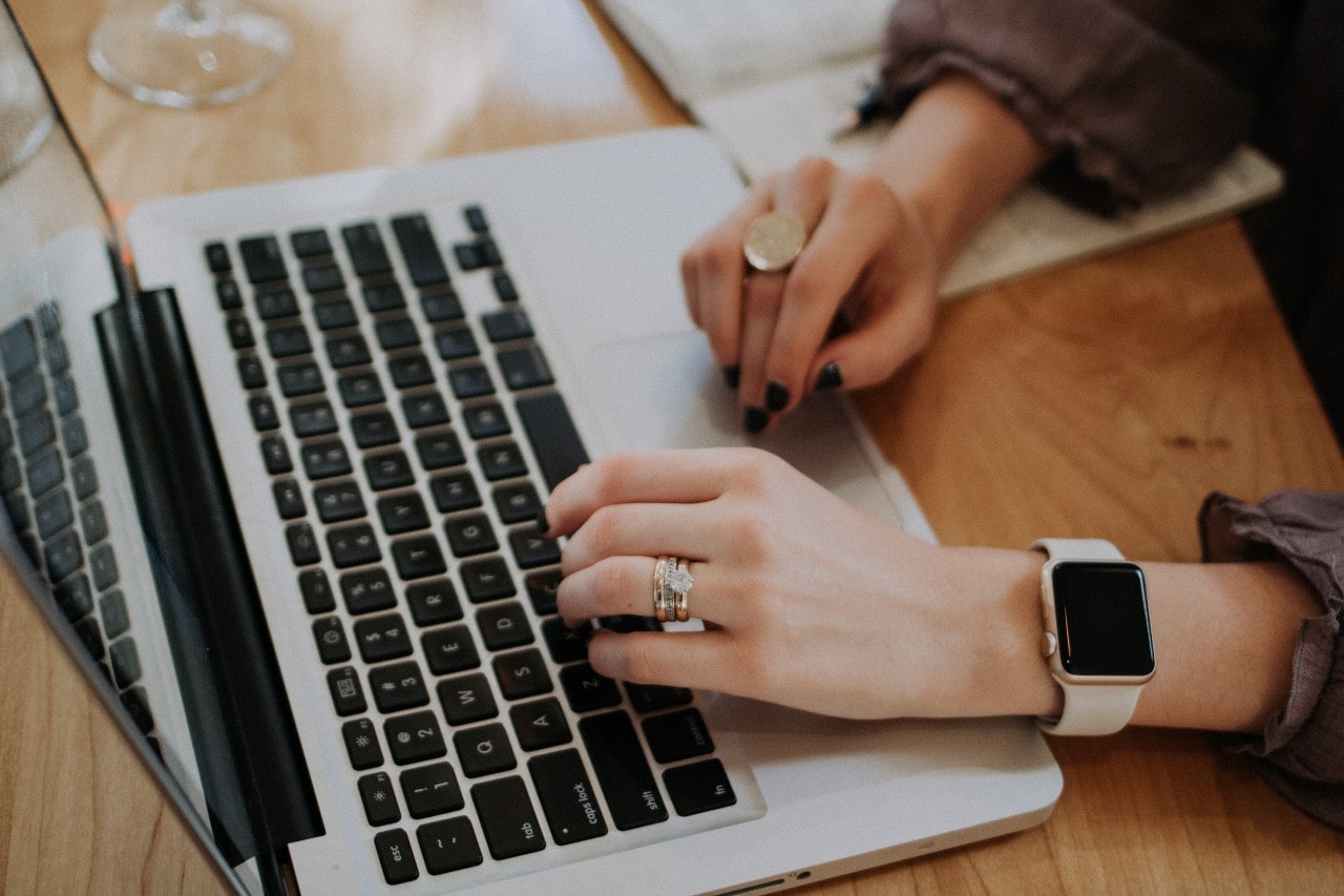 A woman working on her laptop at a table with her wedding band and anniversary band on top of her engagement ring