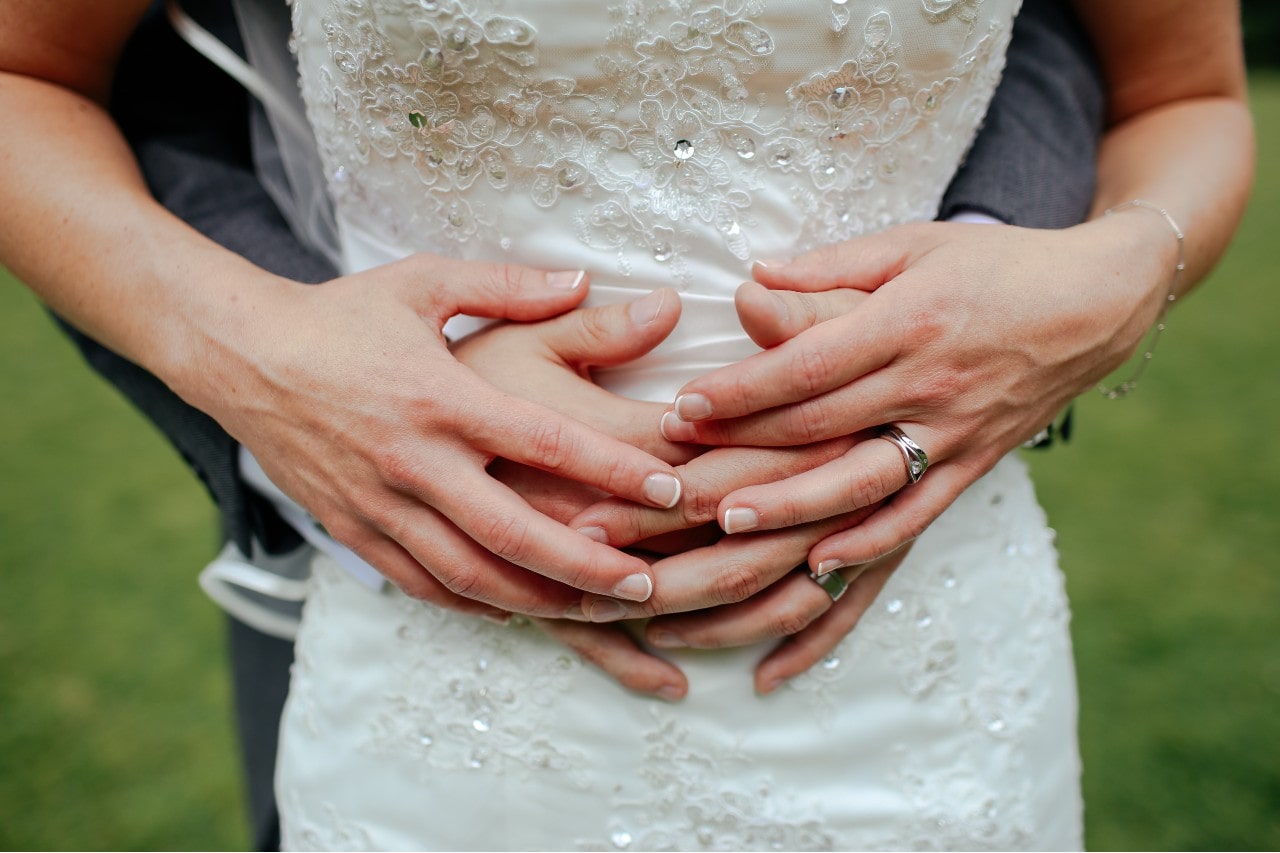 A couple after their wedding with their arms around each other, displaying each of their new wedding rings