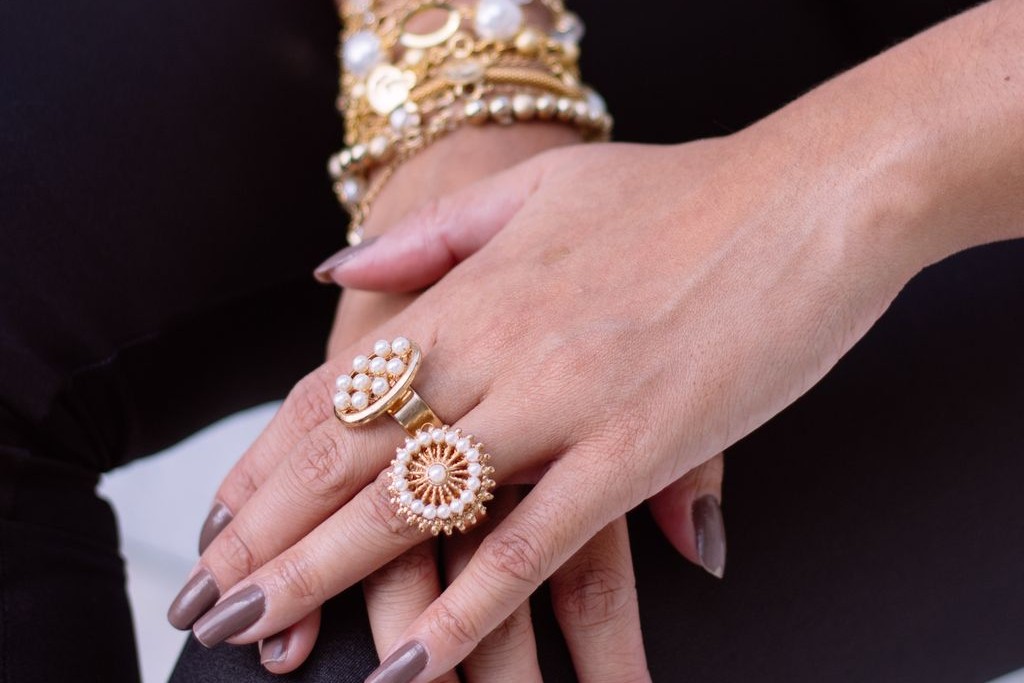 A close-up of a woman’s hands, adorned in many pearl and yellow gold rings and bracelets.