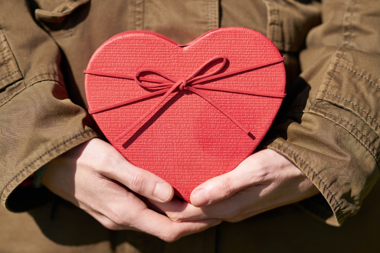 A close-up of a person’s hands holding a heart-shaped gift box.