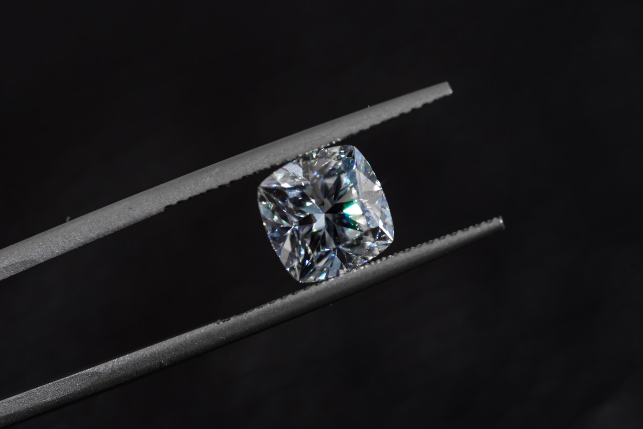 a cushion cut diamond being held between tweezers against a black background