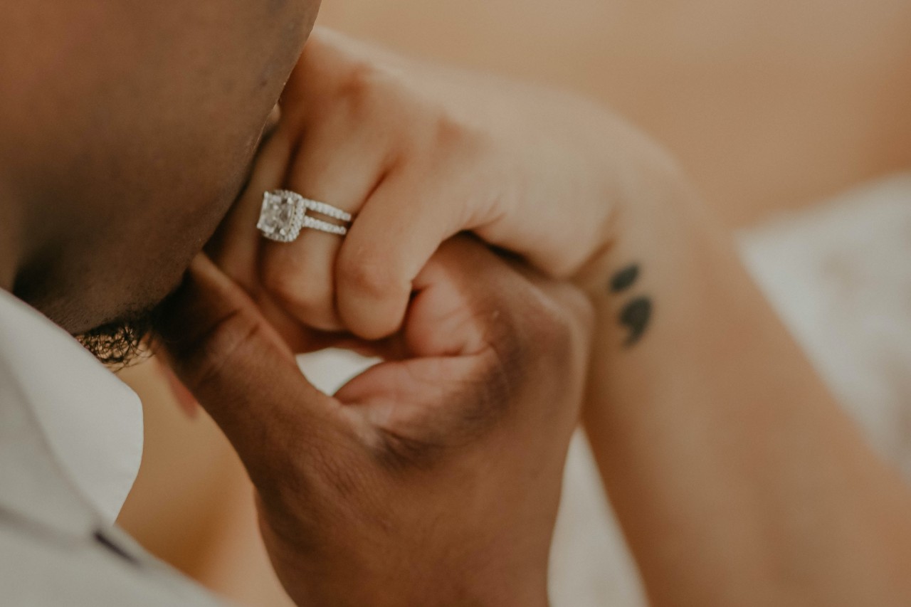 a woman kissing the hand of his bride, who is wearing a white gold halo engagement ring