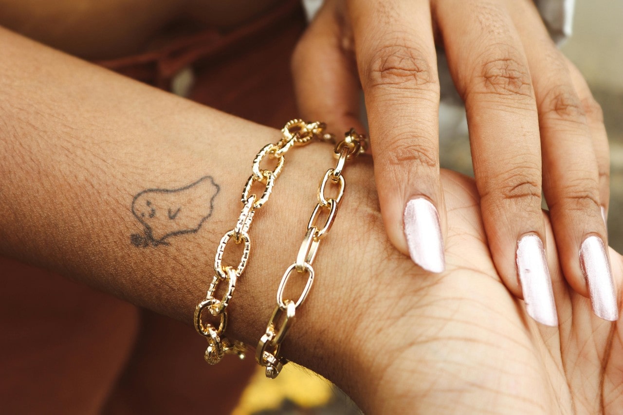 a woman’s wrist adorned with two yellow gold chain bracelets