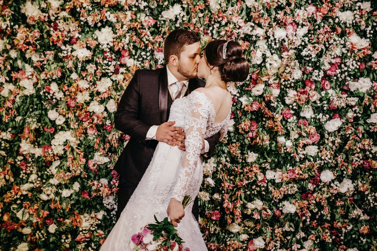 A bride and groom kisses in front of a flower wall.