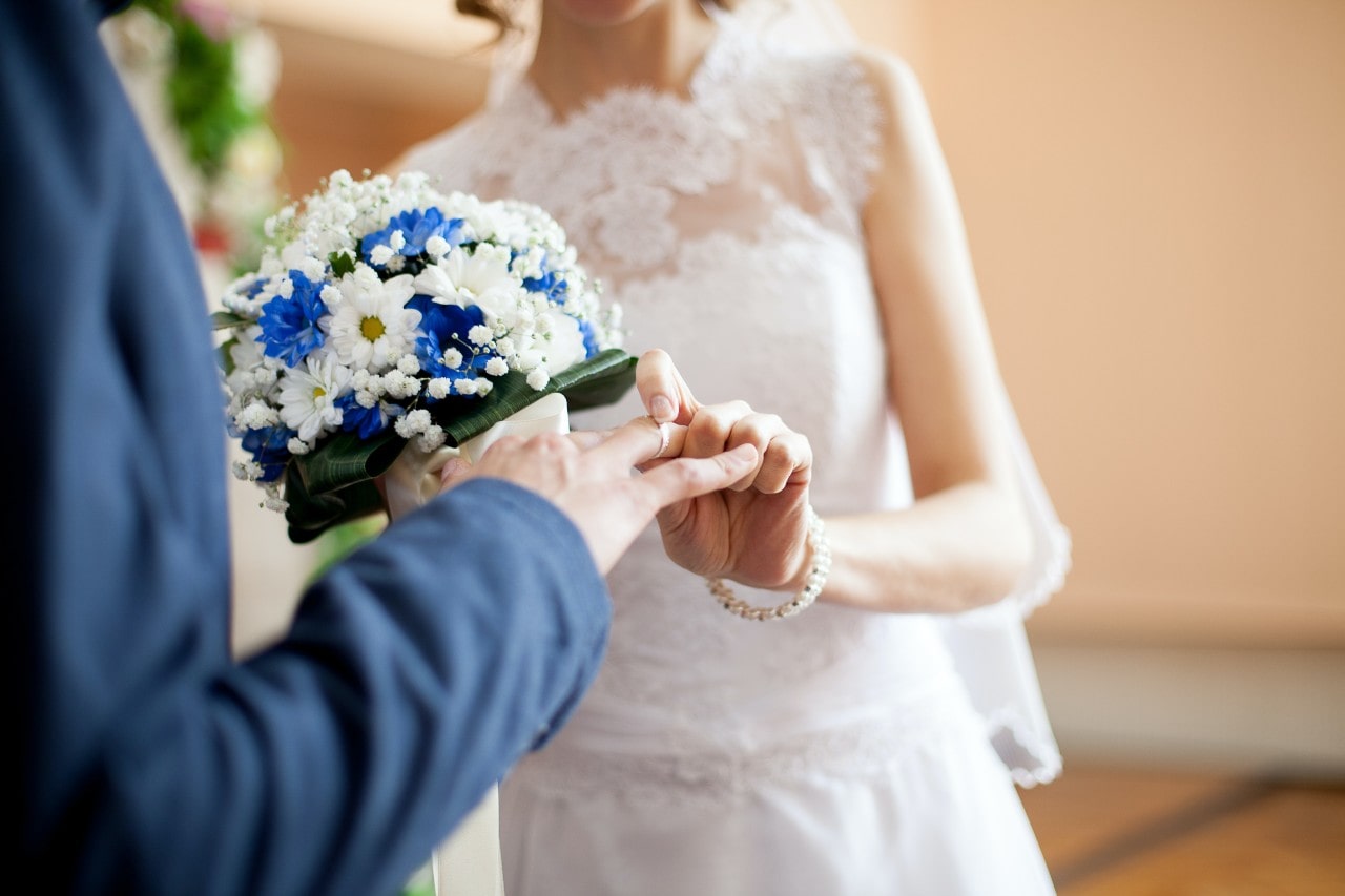 A bride slips a men’s wedding band on her groom’s finger during the ceremony.