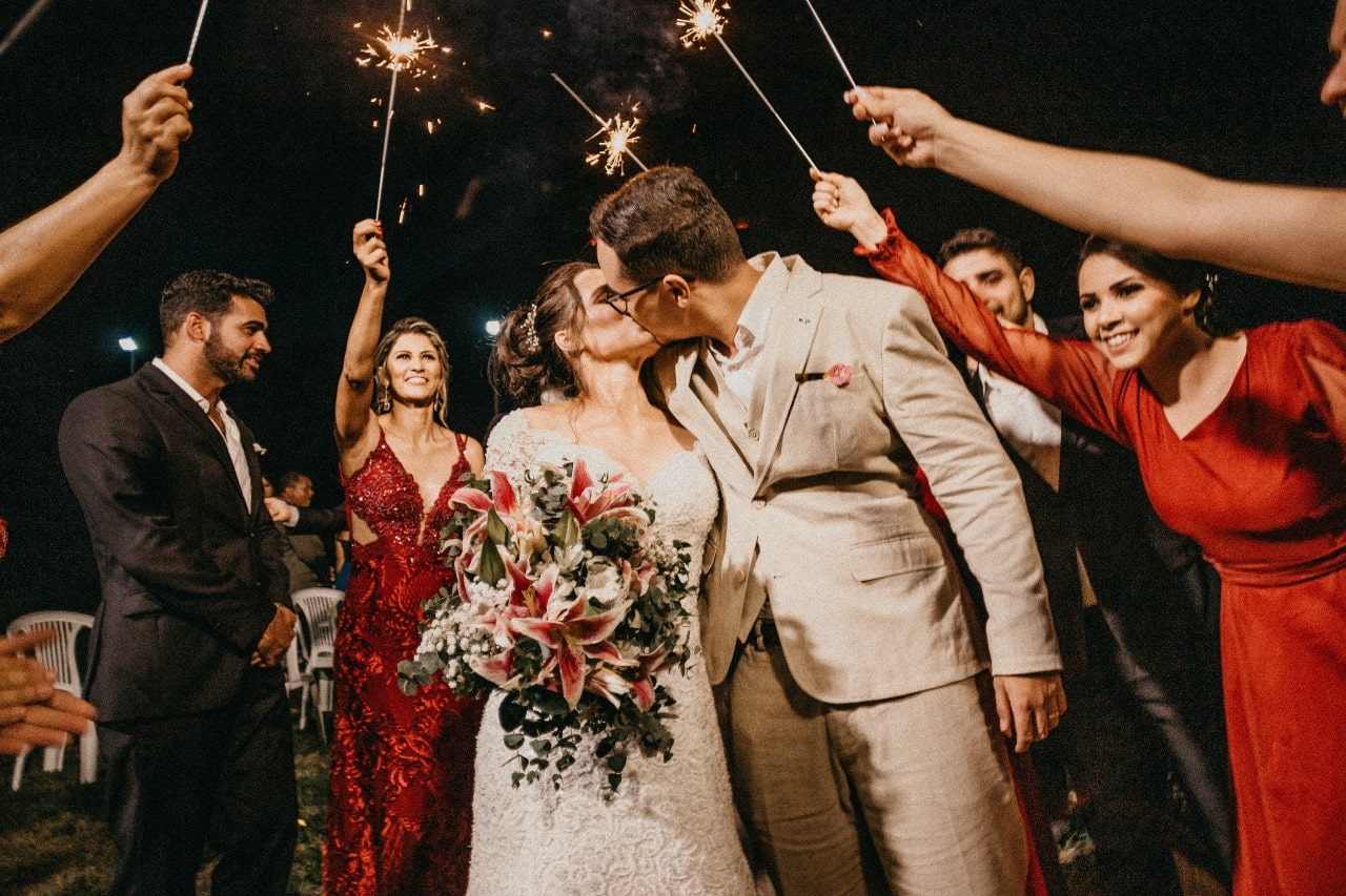 A newly married couple kisses during a grand night time sparkler exit.