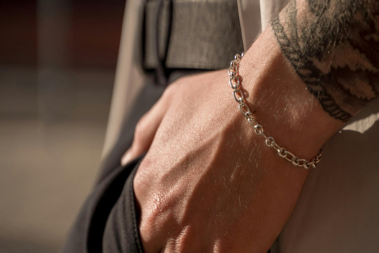 a person’s hand in their pants pocket, wearing a silver chain bracelet