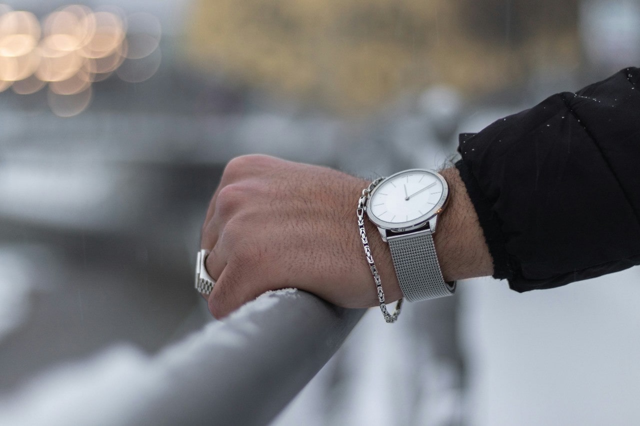 a person’s hand resting on a rail and wearing a silver watch and silver jewelry