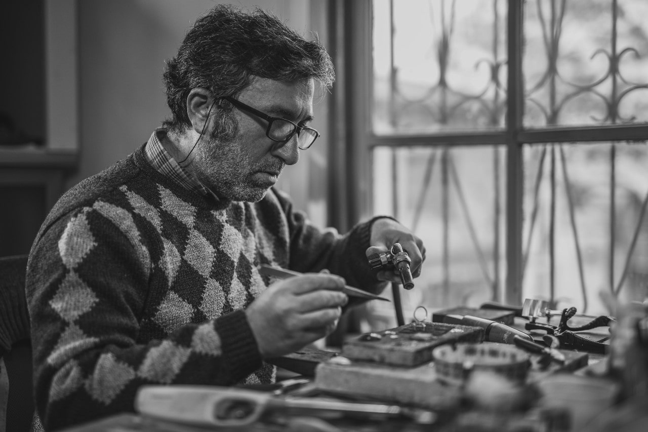 An expert artisan working on a piece of jewelry at his work desk.