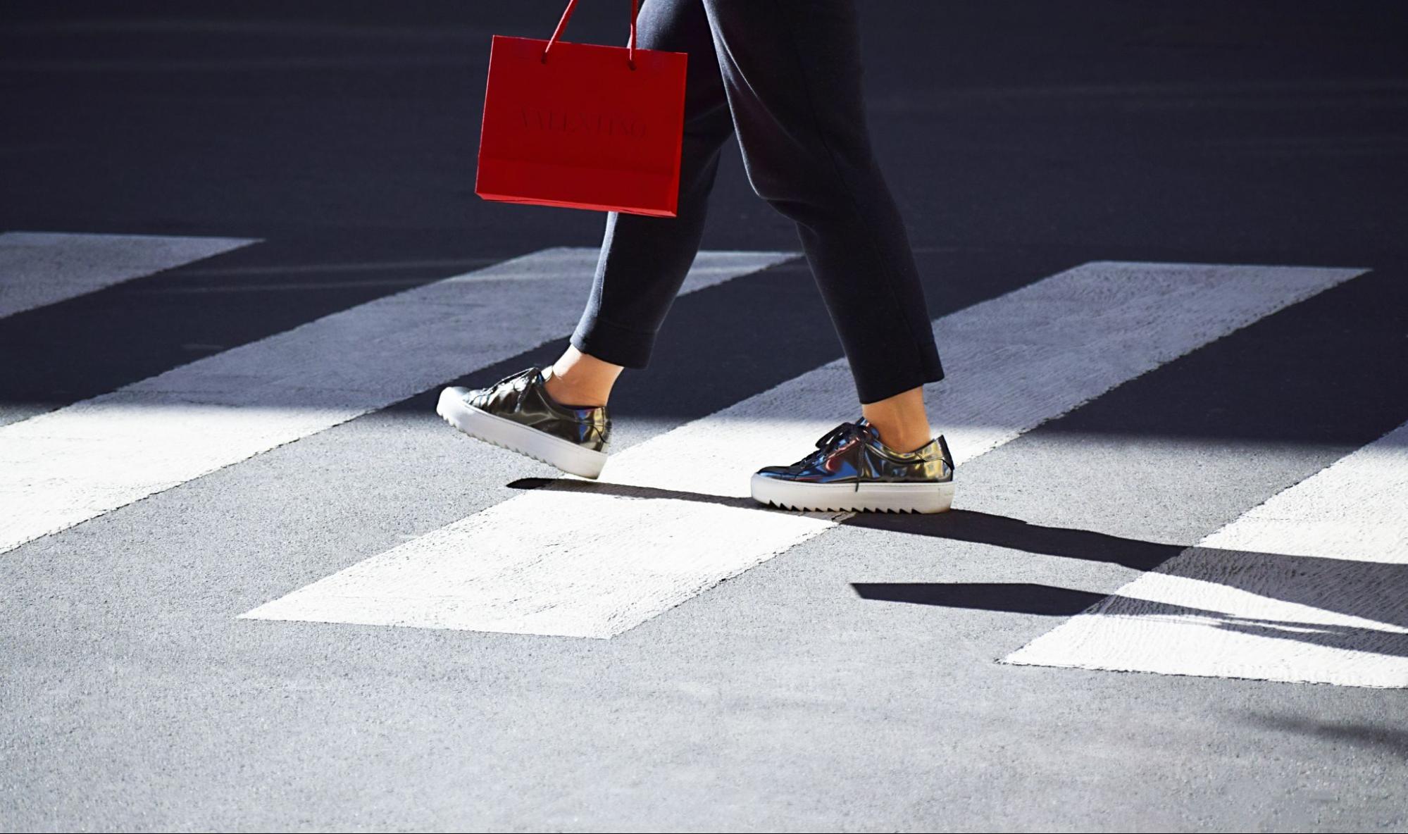 A shot of a casually-dressed woman with a shopping bag crossing the street.