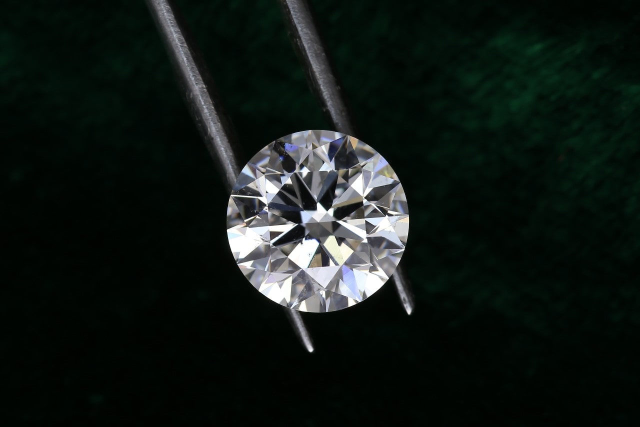 A close-up of a round cut diamond held by jeweler’s tweezers.