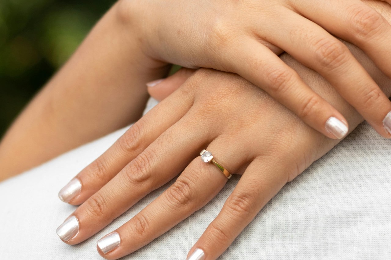 A close-up of a bride’s hands resting on her groom’s shoulder, an engagement ring on one finger.