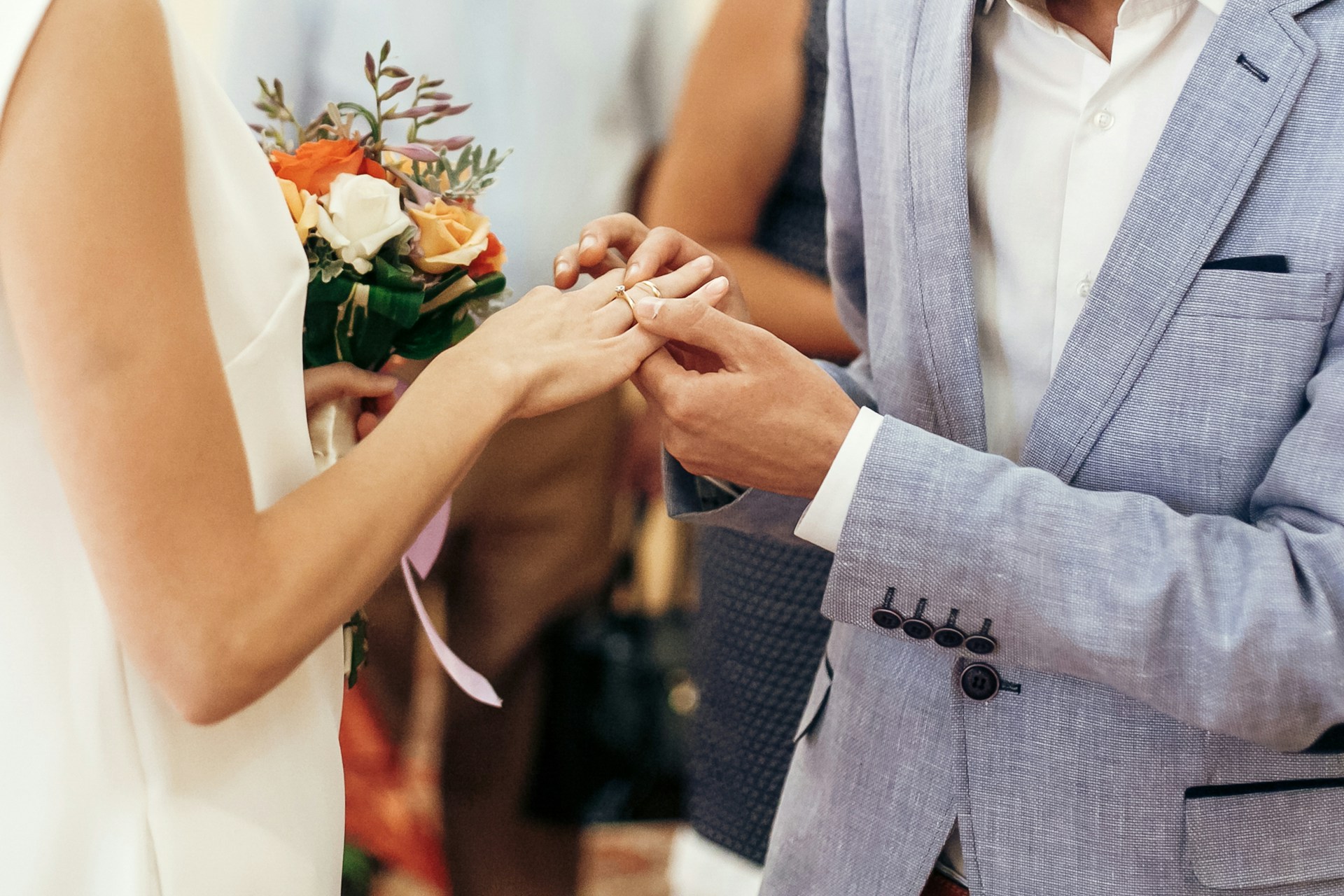 A close-up of a groom putting a wedding ring on his bride’s finger.