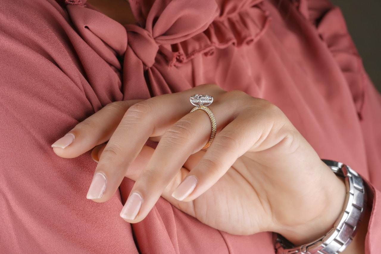 A close-up of a woman’s hand wearing a gold engagement ring.