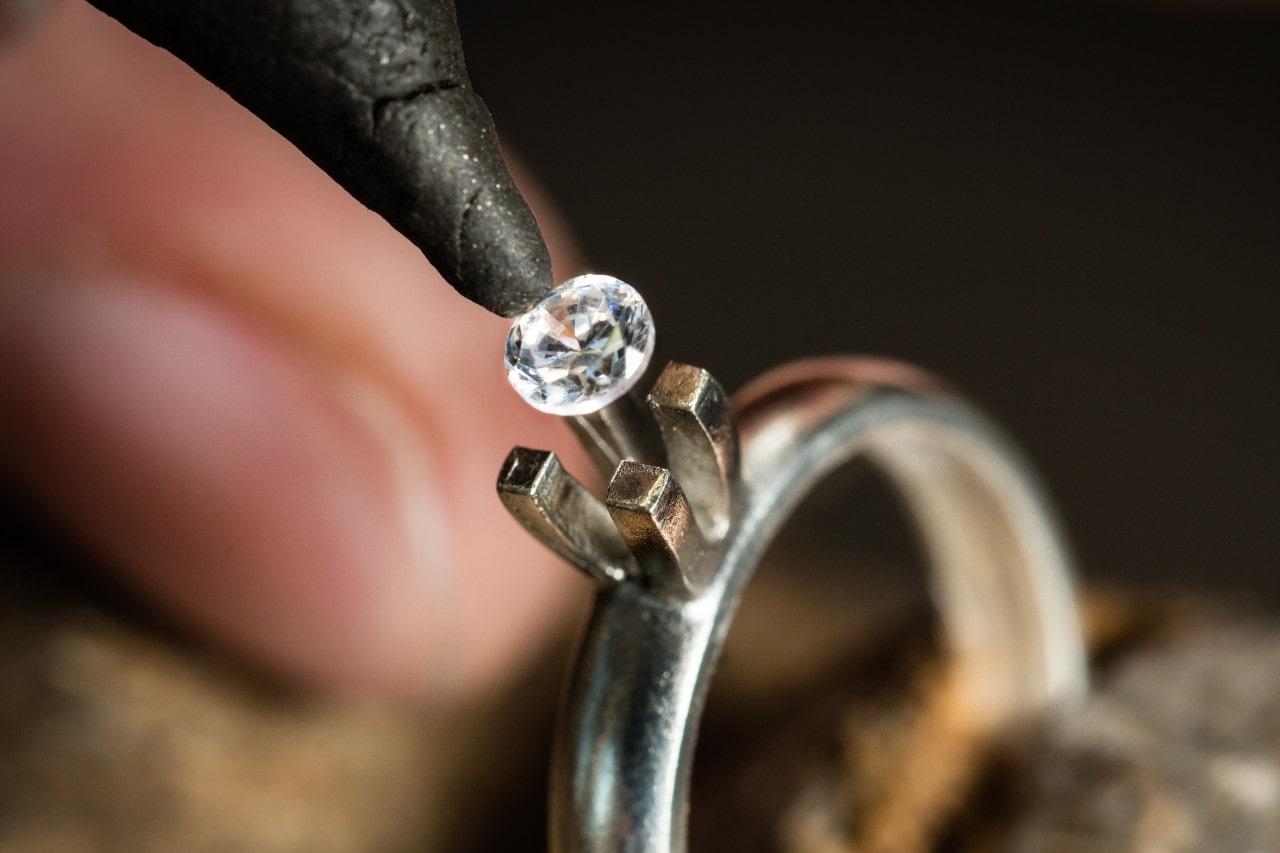 close up image of a diamond being placed into a prong setting on a white gold ring