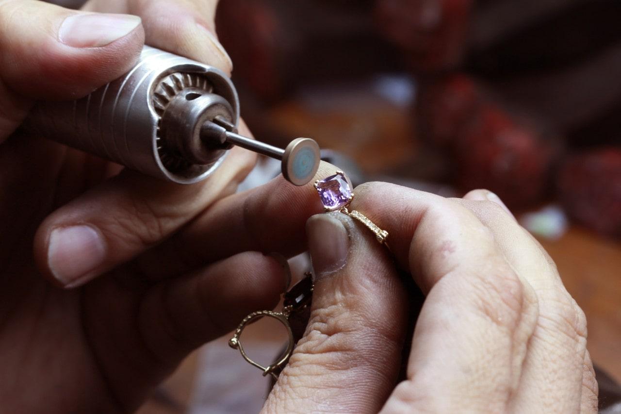 a jeweler’s hands repairing a purple gemstone earring with a round tool