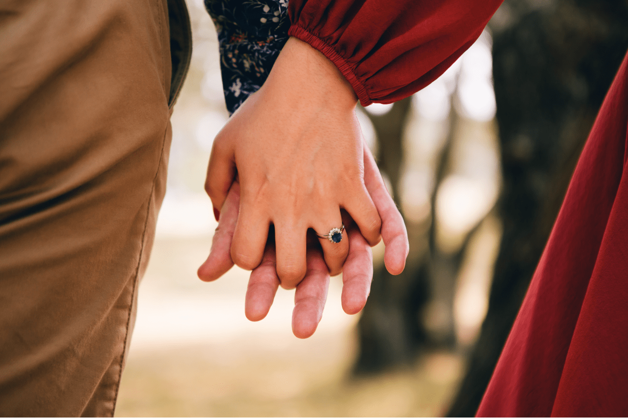 A couple holding hands and you can see the sapphire and diamond halo ring on the woman’s hand.