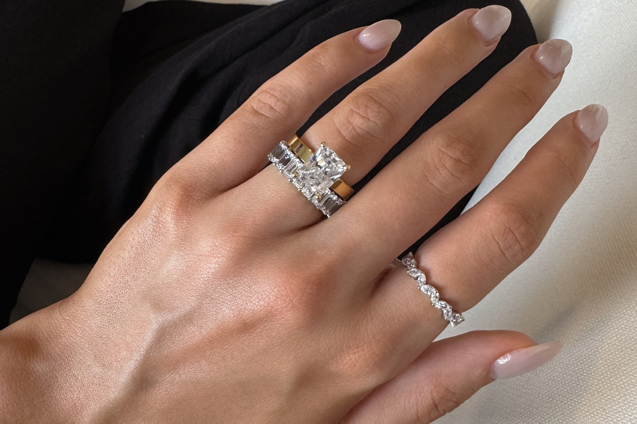 A woman wearing a velvet teal is holding a delicate diamond solitaire engagement ring. A woman wearing a velvet teal is holding a delicate diamond solitaire engagement ring.